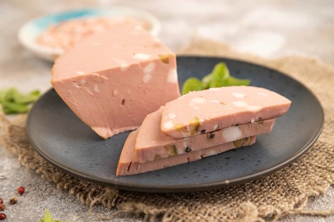 Mortadella sausage on plate with pepper and herbs on brown concrete background and linen textile.