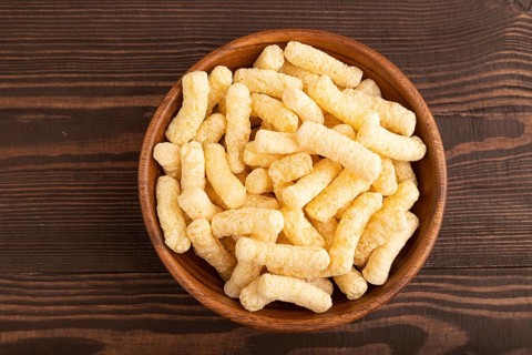 Corn flakes sticks with caramel in wooden bowl on brown wooden background. Top view, flat lay, copy