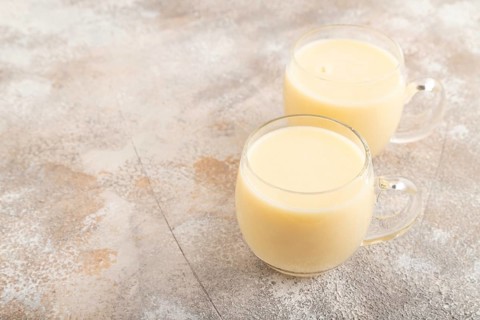 Organic non dairy banana and soy milk in glass on brown concrete background. Vegan healthy food