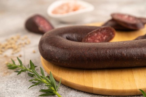 Sujuk sausage on wooden cutting board with pepper and herbs on brown concrete background. Side