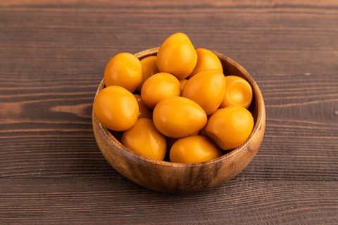 Pile of Smoked Quail eggs in bowl on a brown wooden background. side view, close up