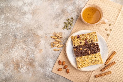 Granola bars with caramel, nuts, flakes in ceramic plate on brown concrete background, beige linen