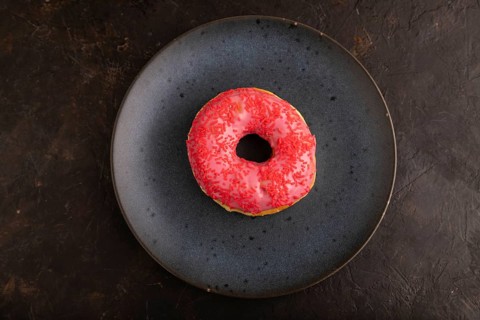 Pink Donut with sprinkles on blue ceramic plate on black concrete background, top view, flat lay,
