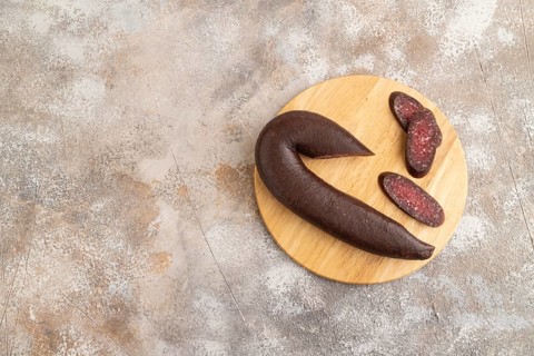 Sujuk sausage on wooden cutting board with pepper and herbs on brown concrete background. Top view,