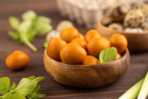 Pile of Smoked Quail eggs in bowl on a brown wooden background. side view, close up, selective
