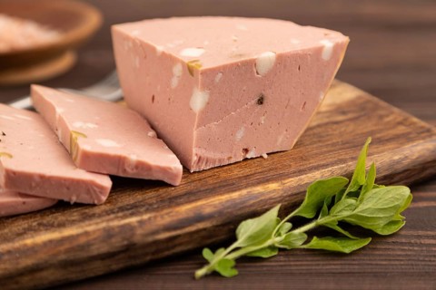 Mortadella sausage on wooden cutting board with pepper and herbs on brown wooden background. Side
