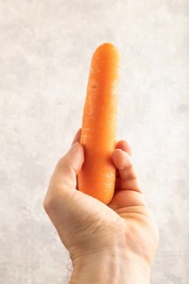 Orange Carrot with hand on gray concrete background. Top view, close up, flat lay. healthy food,