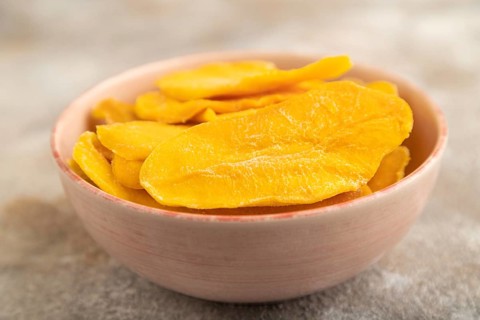Dried Mango in ceramic bowl on brown concrete background. Side view, close up, selective focus.