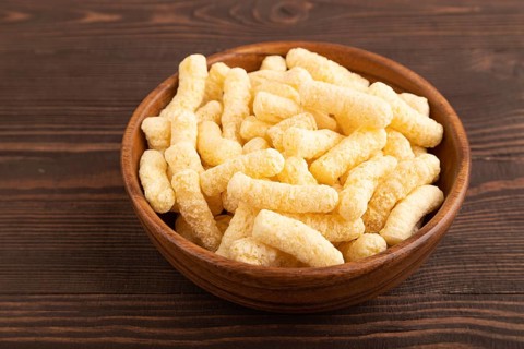 Corn flakes sticks with caramel in wooden bowl on brown wooden background. side view, close up