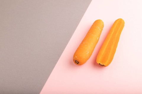 Orange Carrot on gray and pink pastel paper background. Side view, copy space, flat lay. healthy