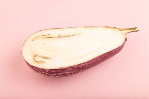 Purple Cutted eggplant with white stripes on pink pastel background. Side view, copy space.