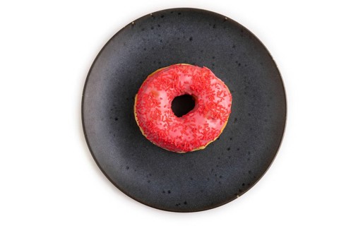 Pink Donut with sprinkles on blue ceramic plate isolated on white background, top view, flat lay,