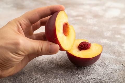 Peach Cut in half with hand on brown concrete background. Side view, copy space. healthy food,