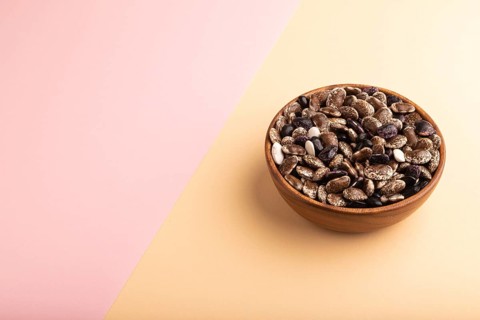 Wooden bowl with Kidney beans on pink and orange pastel paper background, side view, copy space,