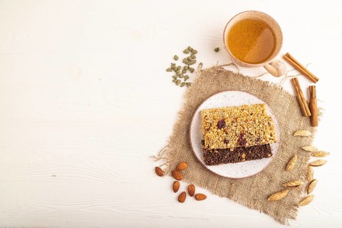 Granola bars with caramel, nuts, flakes in ceramic plate on white wooden background, beige linen