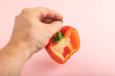 Hand holding sliced Red Cutted pepper on pink pastel background. Side view, copy space. Tropical,