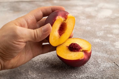 Peach Cut in half with hand on brown concrete background. Side view, copy space. healthy food,