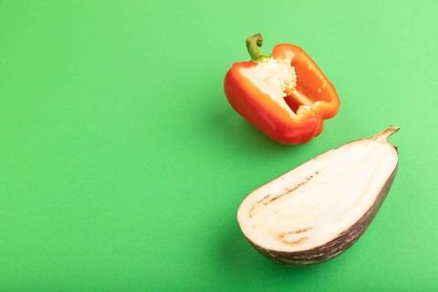Red Cutted pepper and Purple Cutted eggplant on green pastel background. Side view, copy space.
