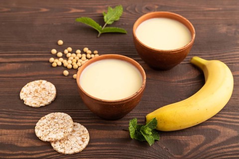 Organic non dairy banana and soy milk in clay cup on brown wooden background. Vegan healthy food
