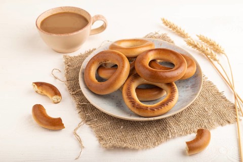 Homemade Ring Bagel with cup of coffee on white wooden background and linen textile. side view,