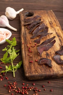 Armenian Basturma dried meat on wooden cutting board with pepper and herbs on brown wooden