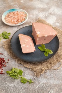 Mortadella sausage on plate with pepper and herbs on brown concrete background and linen textile.