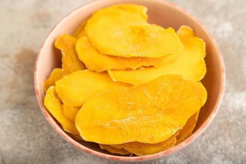 Dried Mango in ceramic bowl on brown concrete background. Side view, close up, selective focus.