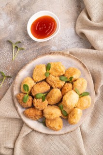 Fried crispy Chicken Nuggets with ketchup, microgreen on brown concrete background and linen