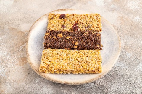 Granola bars with caramel, nuts, flakes in ceramic plate on brown concrete background. Side view,