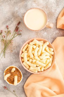 Corn flakes sticks with caramel in ceramic bowl on gray concrete background and orange linen