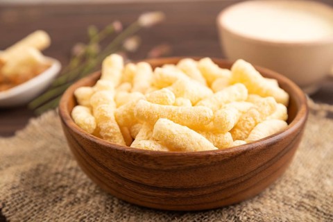 Corn flakes sticks with caramel in wooden bowl on brown wooden background and linen textile. Side