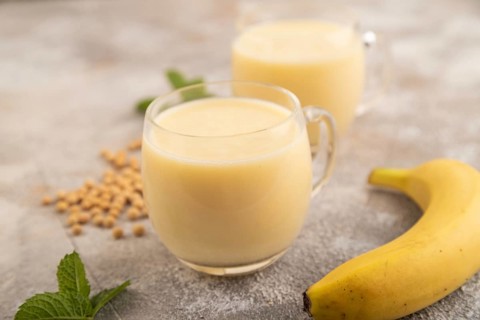Organic non dairy banana and soy milk in glass on brown concrete background. Vegan healthy food