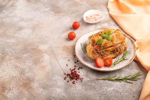 Fried Turkey Thigh with spices and rosemary on plate on brown concrete background and orange linen