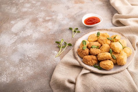 Fried crispy Chicken Nuggets with ketchup, microgreen on brown concrete background and linen