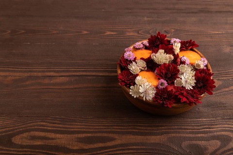 Wooden bowl with carrot slices and red Chrysanthemum flowers, Astrantia flowers, flower salad on