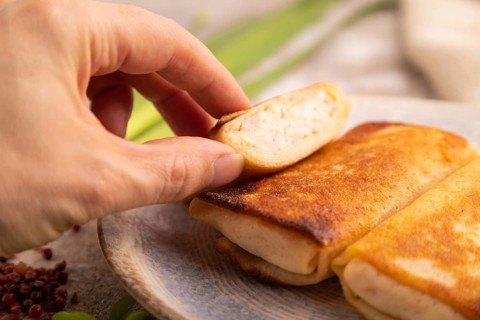Fried crispy pancakes with meat and cheese with hand on brown concrete background and linen textile