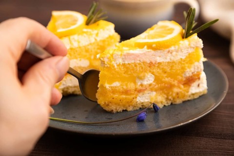 Lemon cake with hand on brown wooden background and linen textile, cup of coffee, side view, close