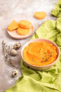 Sweet potato porridge in ceramic bowl on brown concrete background and green textile. Diet, healthy