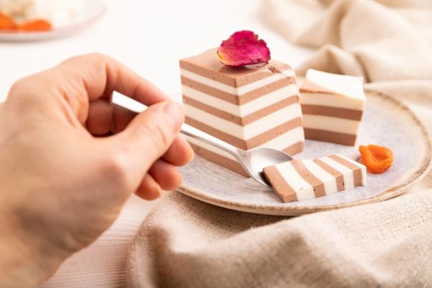 Cocoa and milk jelly with dried apricots with hand on white wooden background and linen textile,