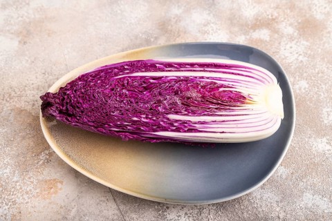 Purple Chinese cabbage on blue plate on brown concrete background, side view, close up, minimalism