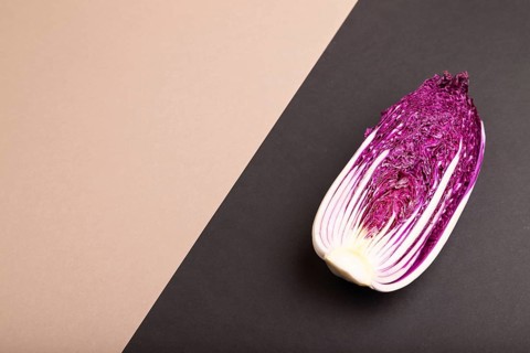 Purple Chinese cabbage on brown and black pastel paper background, side view, copy space,