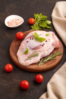 Raw Turkey Thigh with spices and rosemary on cutting board on black concrete background and linen