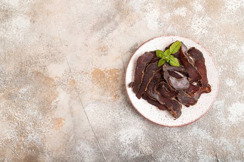 Armenian Basturma dried meat on plate with pepper and herbs on brown concrete background. Top view,