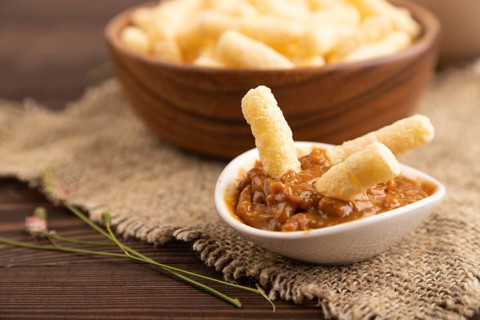 Corn flakes sticks with caramel in wooden bowl on brown wooden background and linen textile. Side