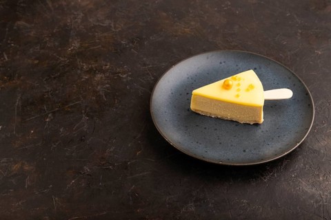 Yellow Cake pop with sprinkles on blue ceramic plate on black concrete background, side view, copy