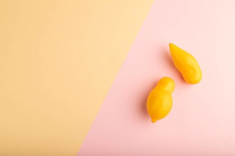 Yellow tomatoes on pink and orange pastel paper background. Top view, copy space, flat lay. healthy