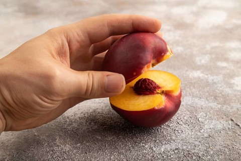 Peach Cut in half with hand on brown concrete background. Side view, copy space. healthy food,