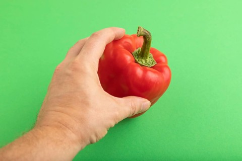 Hand holding Red pepper on green pastel background. Side view, copy space. healthy food, vegetable,