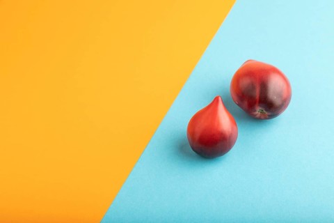 Red Heart shape tomatoes on blue and orange pastel paper background. Side view, copy space. healthy