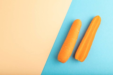 Orange Carrot on orange and blue pastel paper background. Top view, copy space, flat lay. healthy